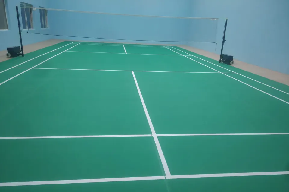 Close view of white court lines on a green badminton mat, with a post and net in the background.
