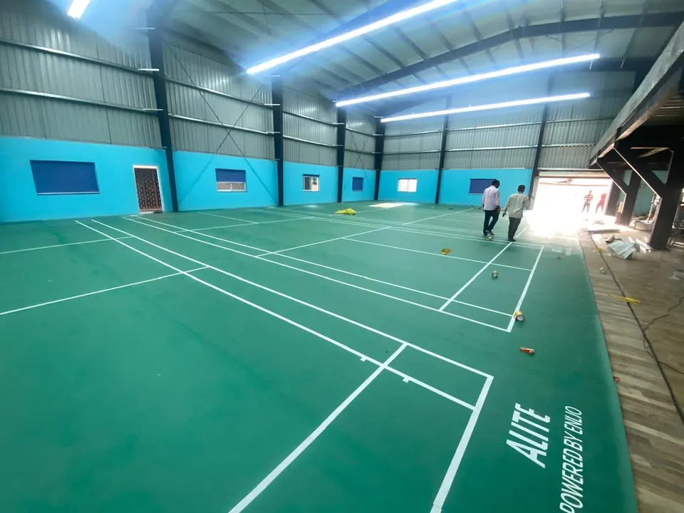 Badminton court mats being finished in a large multi-court hall, with line-marking tape still on the floor.