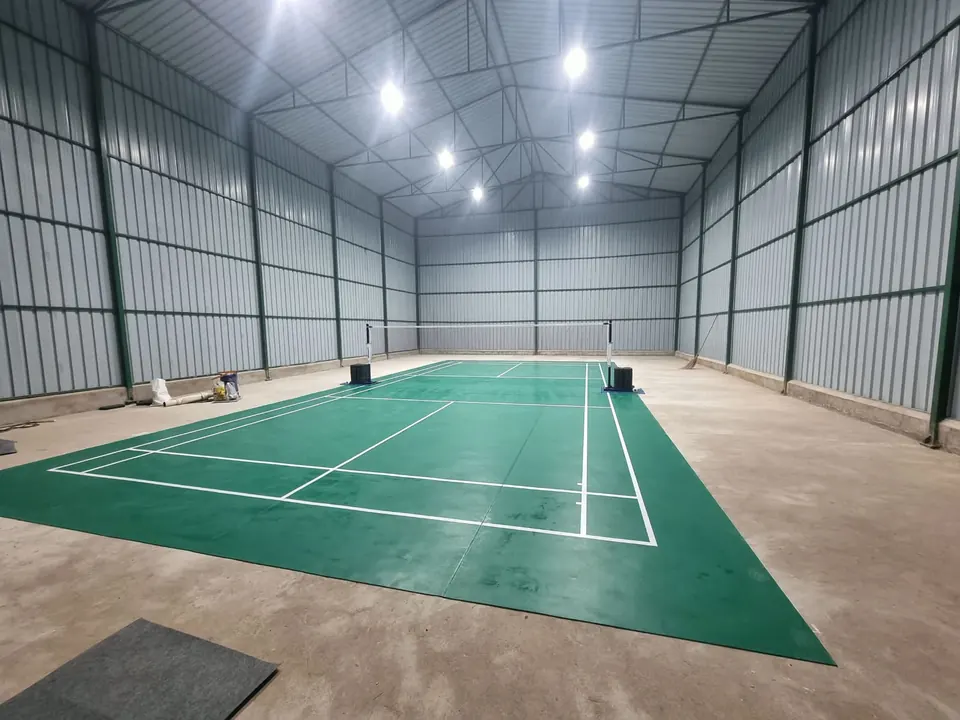 Newly laid green badminton court mat inside a steel-framed shed built by Kelysports, with high-bay LED lights.