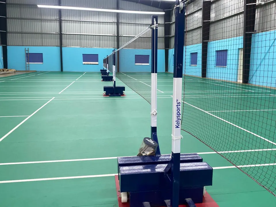 Badminton posts manufactured in-house by Kelysports, with weighted bases holding a net across a multi-court indoor hall.
