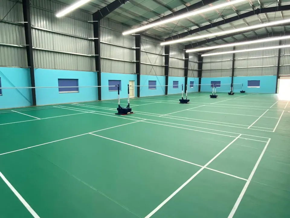 Row of indoor badminton courts built by Kelysports in a steel-roofed hall with light blue walls, posts, nets and linear LED lights.