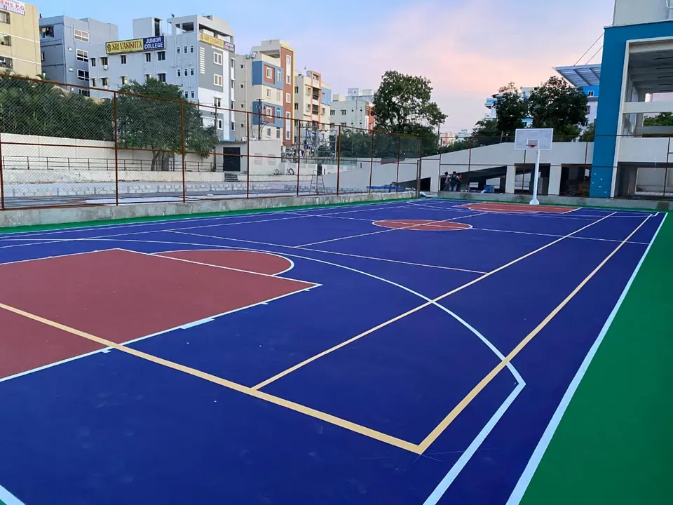 Close view of an outdoor acrylic basketball court in deep blue with a red key, white and yellow lines and a pole at the far end.