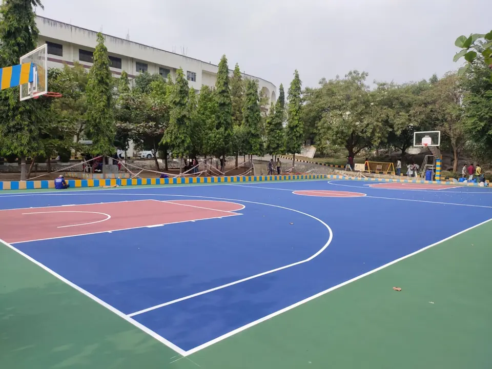 Basketball court construction by Kelysports: an outdoor acrylic court in blue with red keys and a green surround, with poles at both ends and trees behind.