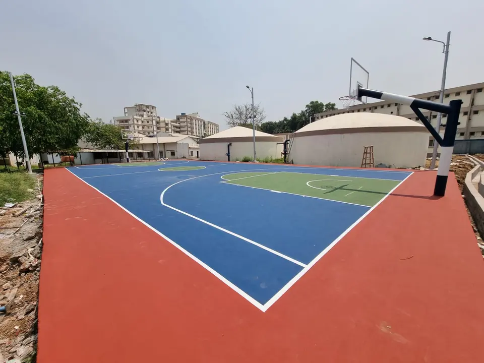 Newly finished outdoor acrylic basketball court with a blue playing area, green key and red surround, with the backboard and pole fitted.
