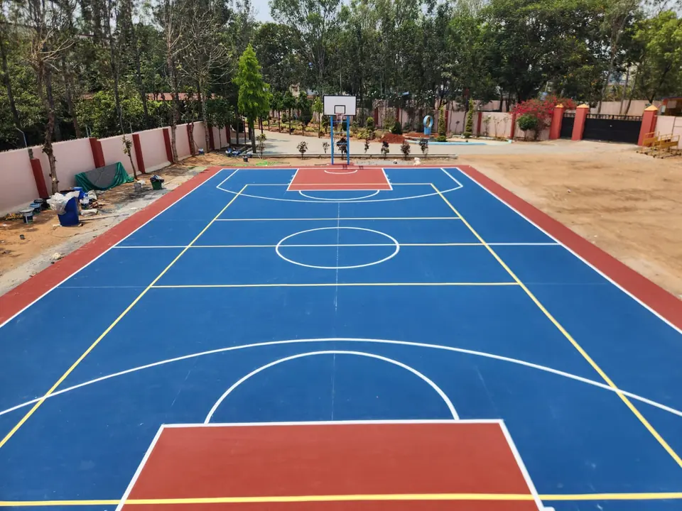Kelysports team at work beside an outdoor acrylic basketball court in blue and red with yellow multi-sport lines and a pole at the far end.