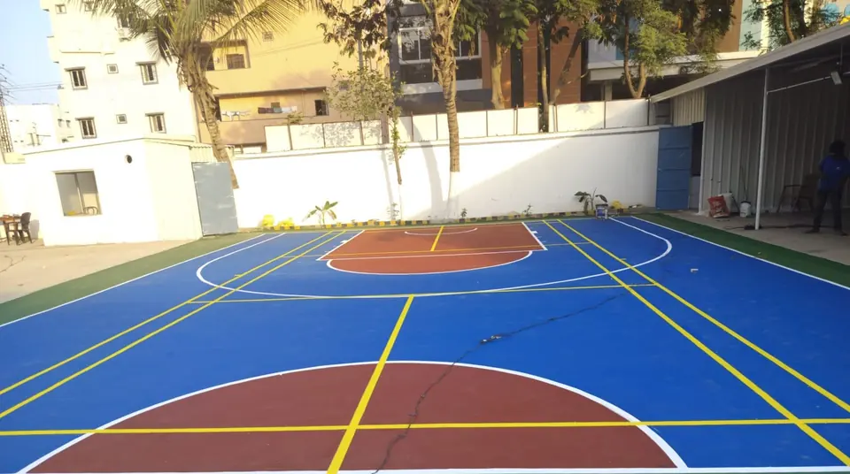 Outdoor acrylic basketball court in blue with red keys and a green surround, marked with extra yellow lines for other sports.