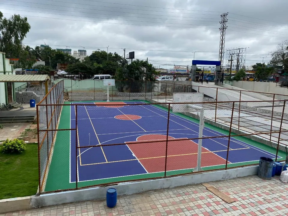 Fenced outdoor acrylic court marked for basketball, with extra coloured lines for other sports and poles at both ends.