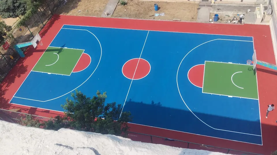Aerial view of a full outdoor acrylic basketball court in blue with a red surround, green keys and both poles in place.
