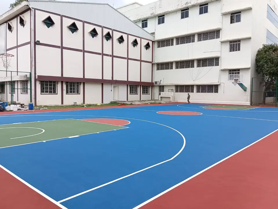 Outdoor acrylic basketball court with blue playing areas, a green key and red surround, in front of a large building block.