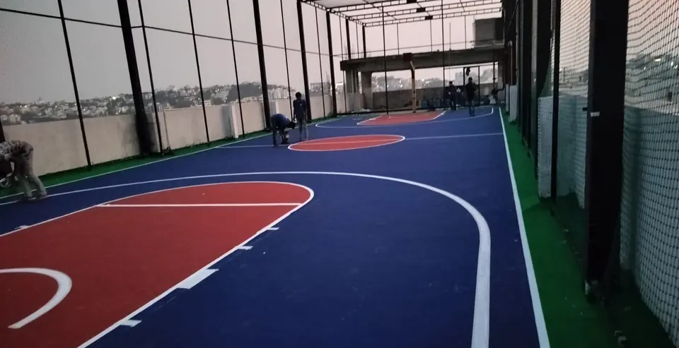 Rooftop basketball court in navy blue and red inside a netted enclosure, with the Kelysports team finishing the line marking.