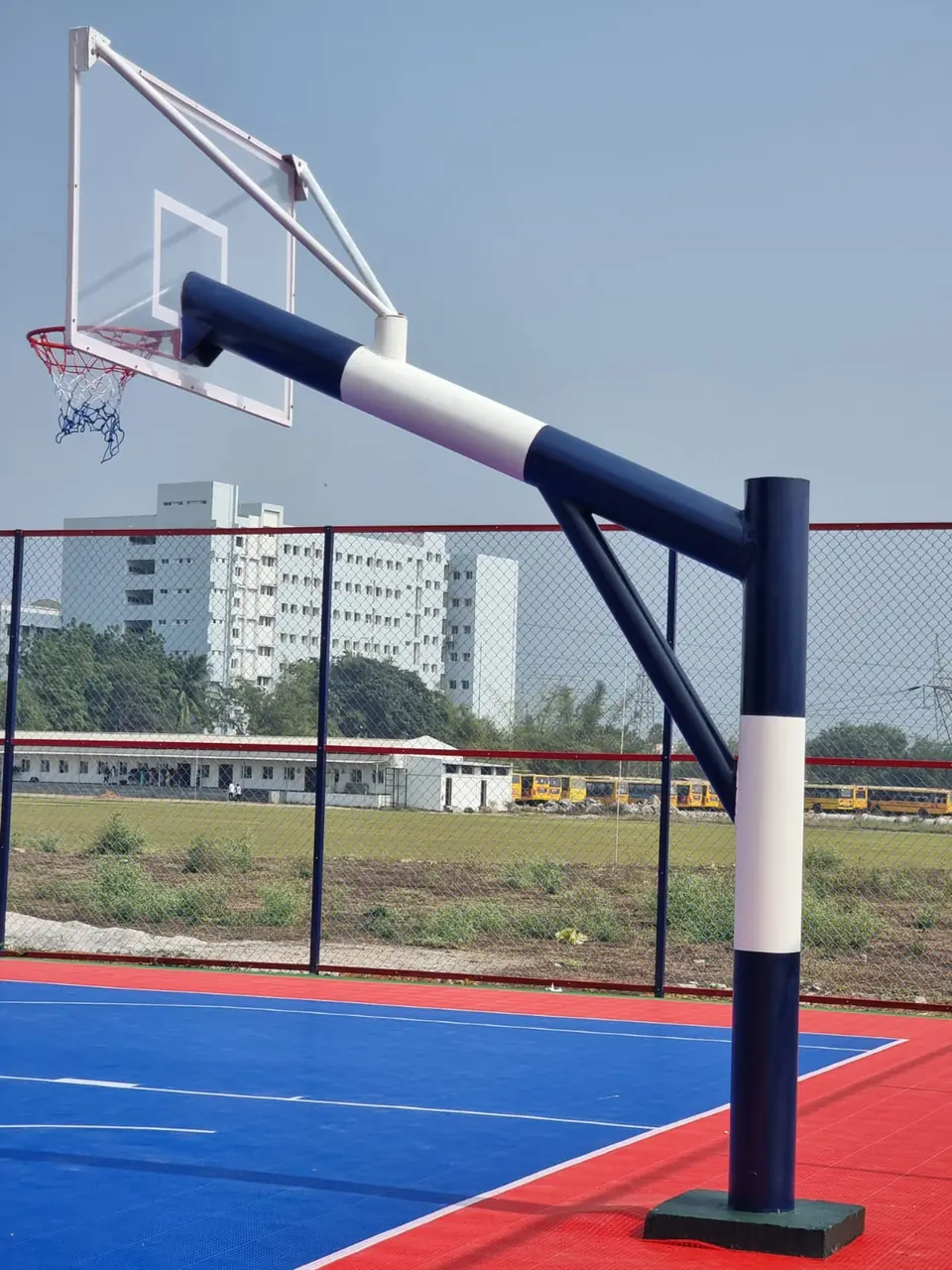 Blue and white Kelysports basketball goal post with a braced backboard, ring and net over a blue and red interlocking tile court.