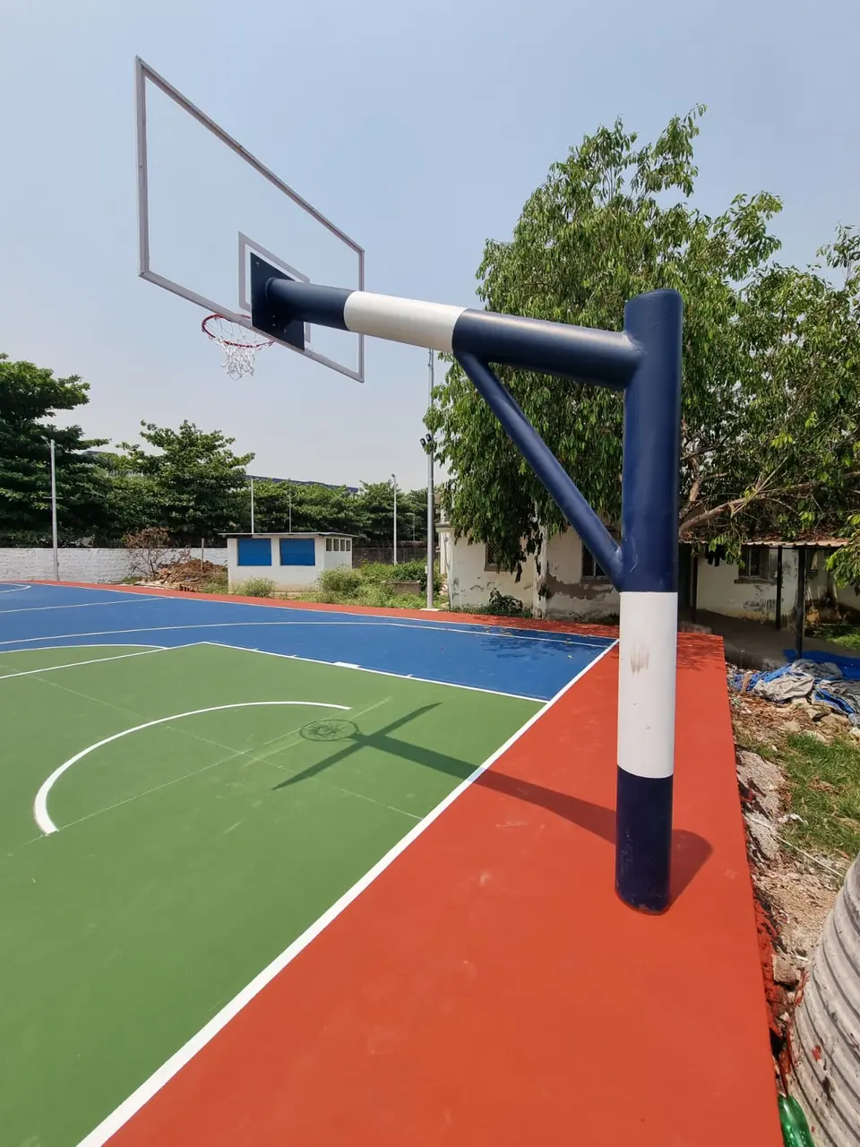 Kelysports basketball pole with a braced extension arm holding the backboard, ring and net over a blue, green and red court from outside the boundary line.