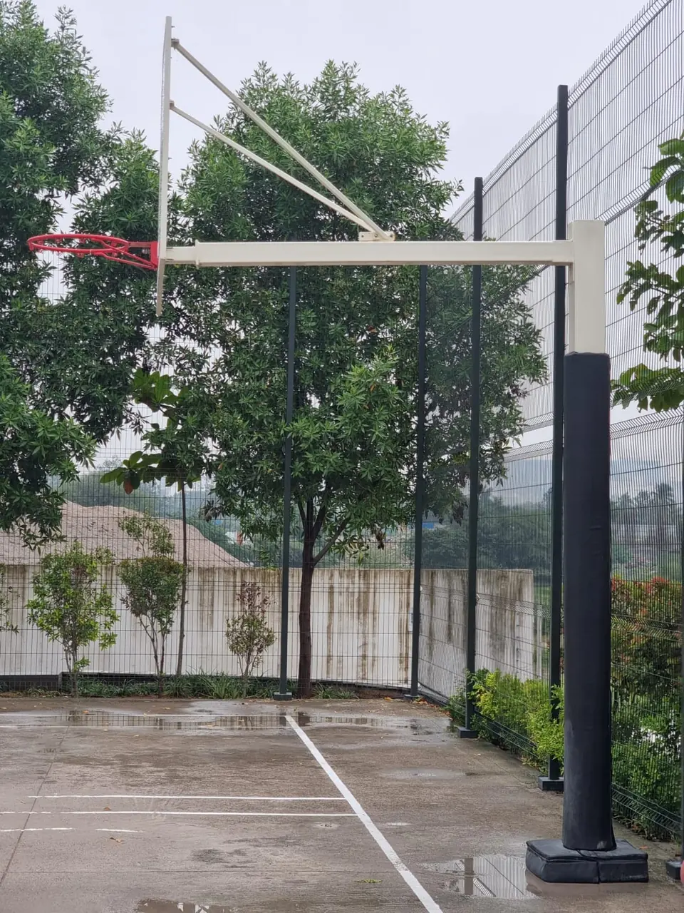 Side view of a Kelysports basketball pole with a square post, long horizontal extension arm and braced backboard, on an outdoor concrete court.