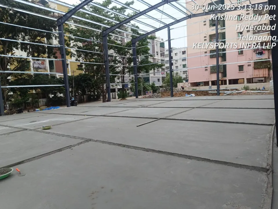 Freshly finished concrete base slab laid in panels with joints, inside the steel frame of a sports shed.