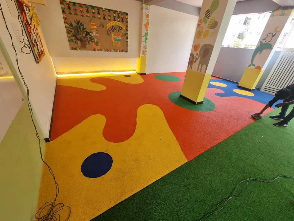 Orange, yellow and blue EPDM flooring with circle inlays meeting artificial turf in a covered play area.