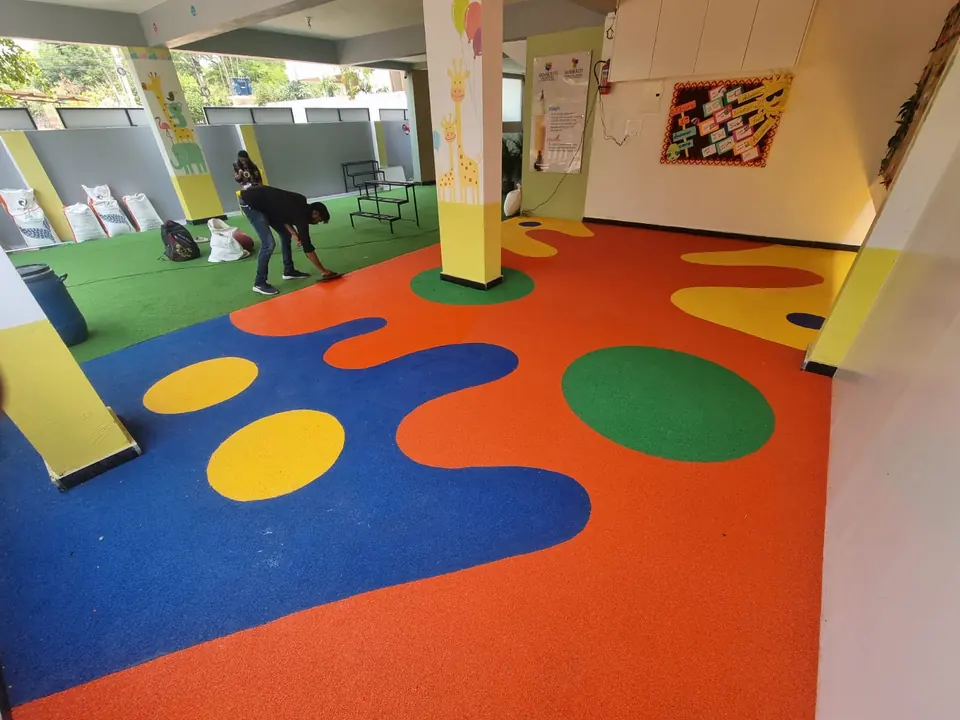Workers finishing an orange, blue and yellow EPDM floor in a covered play area.