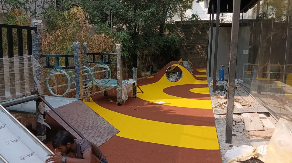 EPDM flooring installation in progress on a play area with yellow and brown curved bands and a play mound.