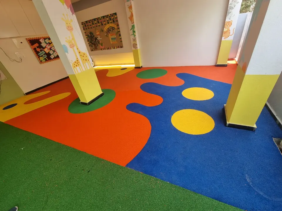 Covered play area with orange and blue EPDM flooring, yellow and green circles and an artificial turf strip.