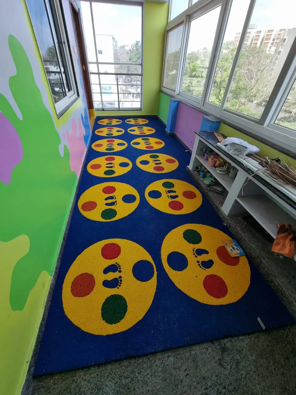 Blue EPDM floor with yellow footprint-game circles along a play balcony.
