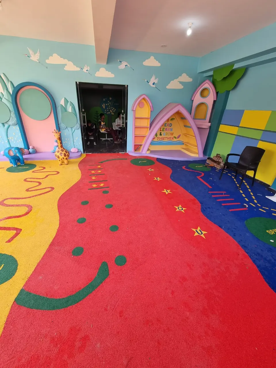 Indoor children's play area with red, yellow and blue EPDM flooring and themed wall features.