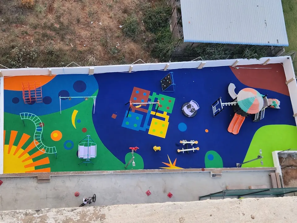 Top-down view of a long play area with blue, green and orange EPDM flooring and several play features.