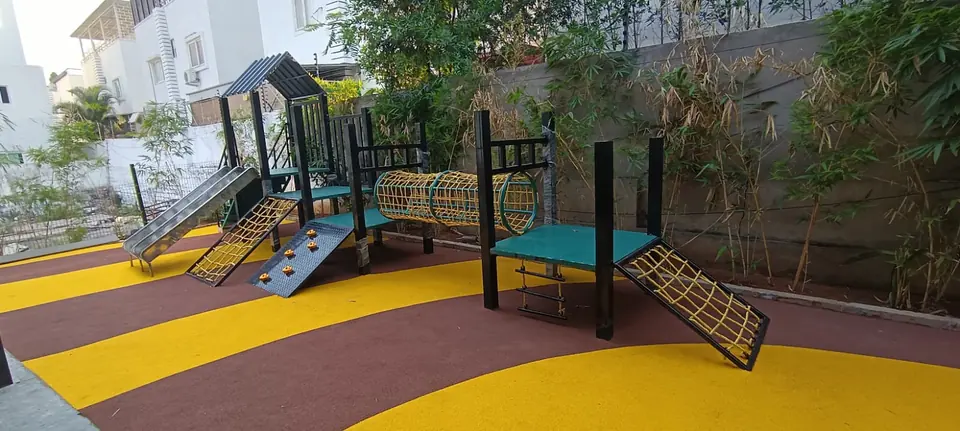 Brown and yellow swirl-pattern EPDM flooring by Kelysports around a play structure with a tunnel and climbing net.