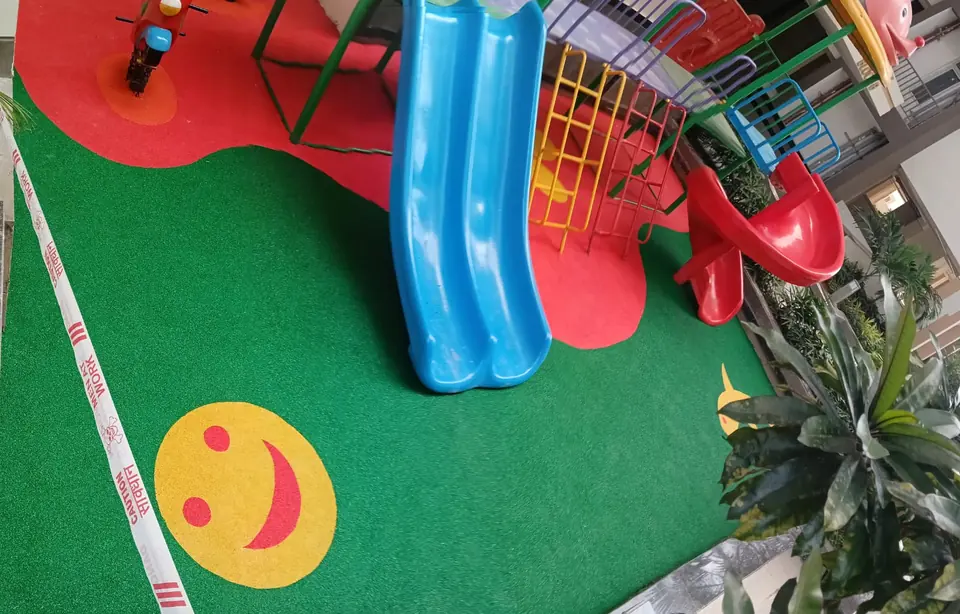Close view of green EPDM flooring with a yellow smiley-face inlay beside blue and red slides.