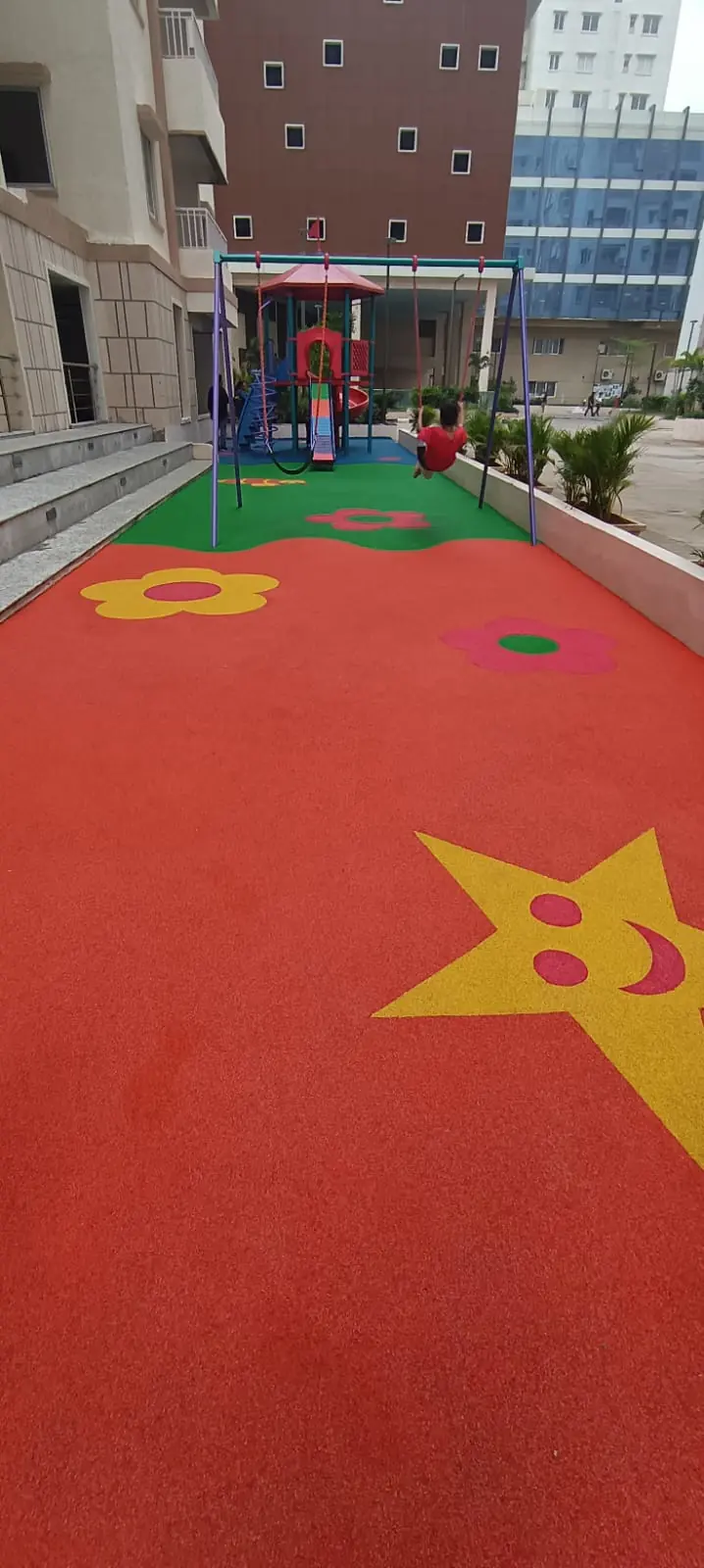 Red EPDM play area flooring with a smiling star and flower inlays, with a playset in the background.