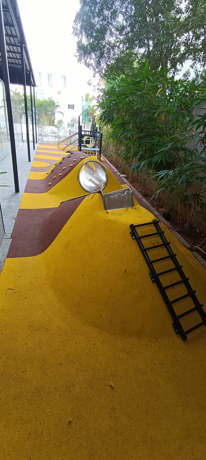 Yellow EPDM rubber surface over a play mound with a stainless steel slide and ladder.
