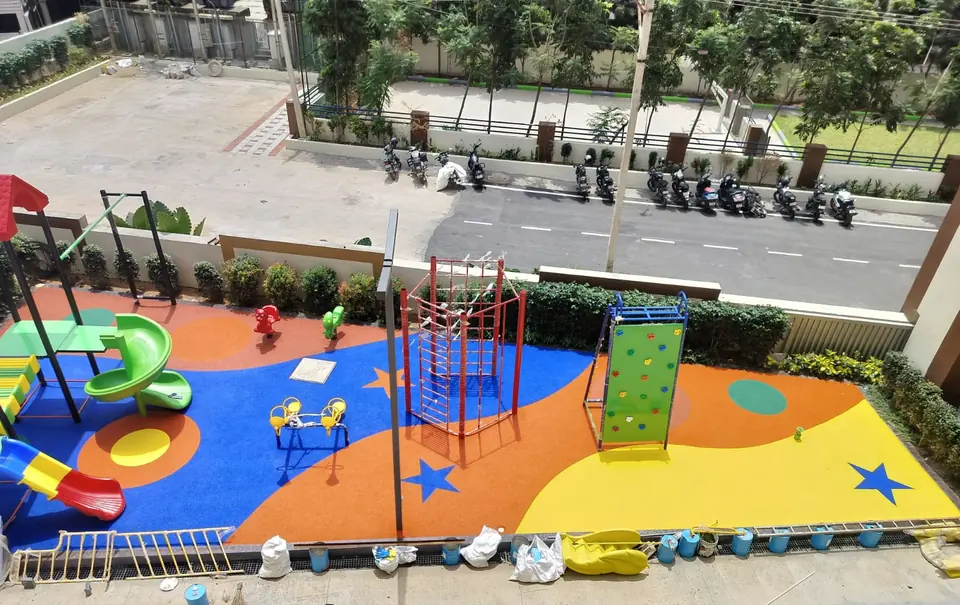 Playground with blue, orange and yellow EPDM flooring, a climbing frame and a spiral slide, seen from above.