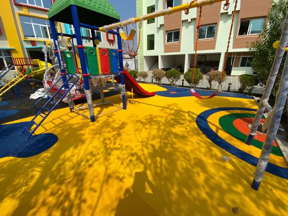 Yellow EPDM playground flooring with blue and green accents under a playset and swings.