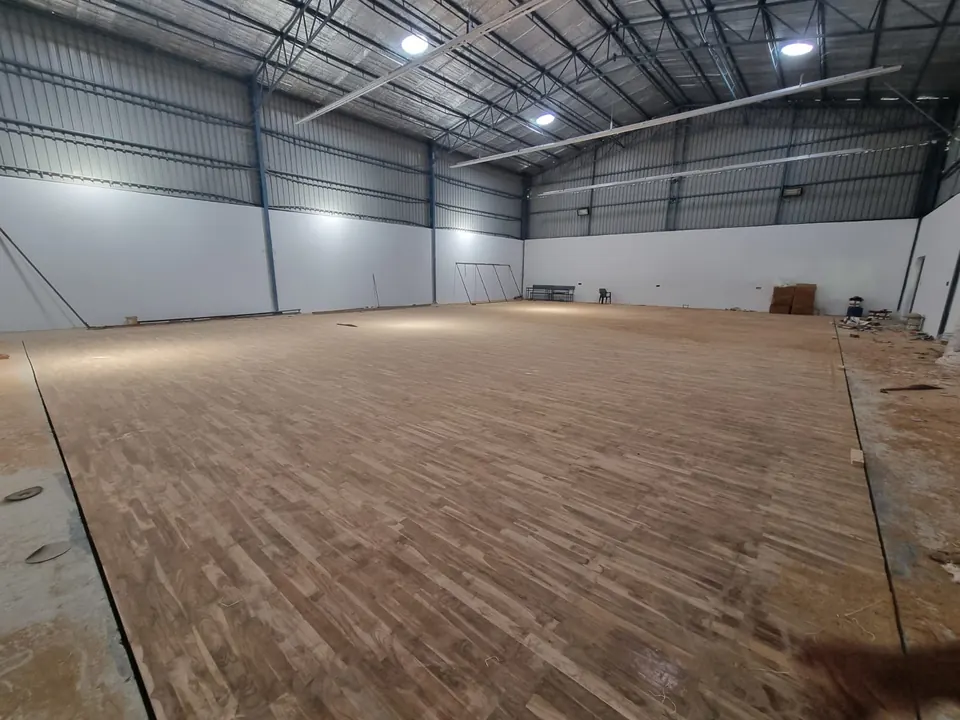 Teak wooden sports floor laid across the full width of the Kalwakurthy badminton hall, boards running lengthways, before finishing, under the steel roof.