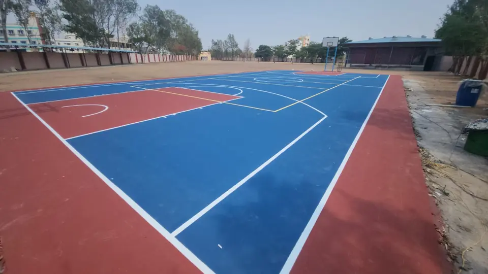 Outdoor acrylic basketball court in blue with a red key and surround, white and yellow line markings for more than one sport, and a basketball pole at the far end.