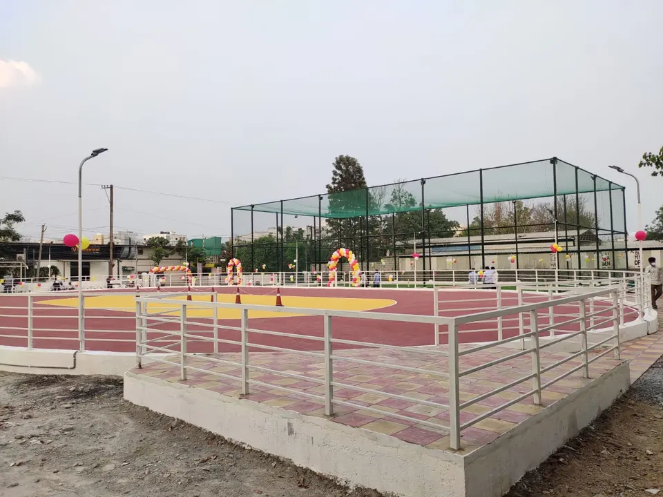 Skating rink seen from a raised concrete platform with steel railings, showing the yellow centre, the maroon track and a netted arena behind.