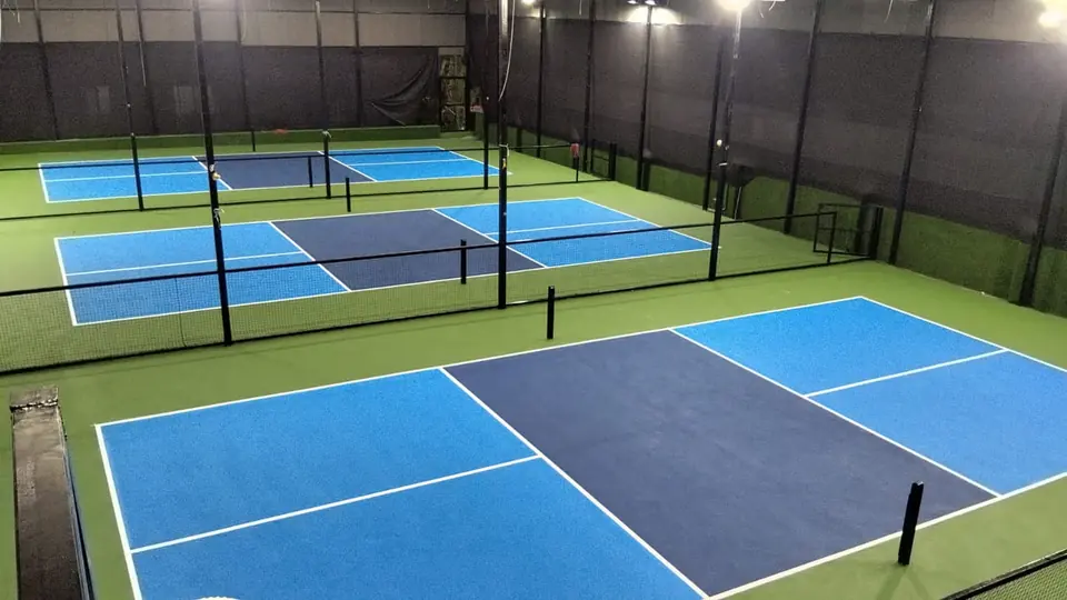 Indoor pickleball facility with three courts in light and dark blue, separated by netting, under high-bay lights.