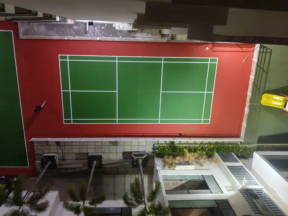 Overhead view of an outdoor badminton court with a green playing area and red surround on a residential podium.