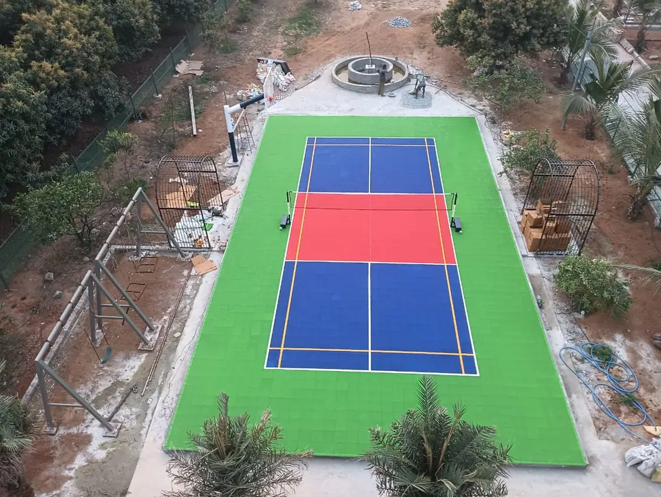 Pickleball court on green, blue and red interlocking tiles in landscaped grounds, with yellow badminton lines and net posts fitted.
