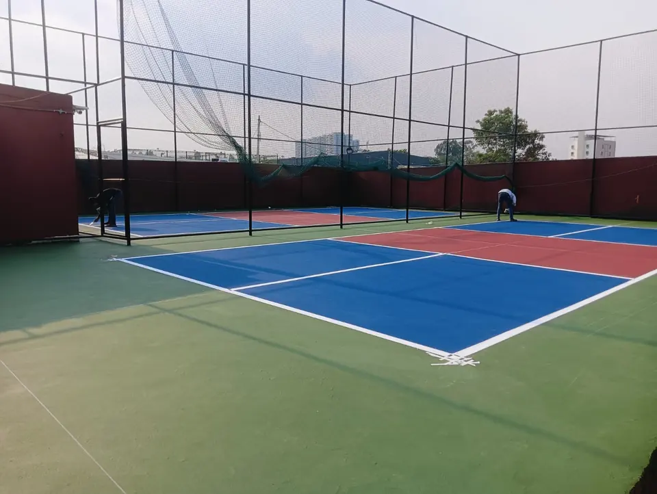 Worker finishing the line marking on a netted outdoor pickleball court with blue and red playing zones.