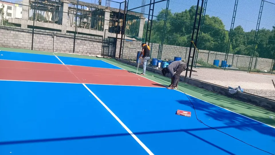 Kelysports team finishing the surface of an outdoor pickleball court, with a blue playing area, red kitchen zone and green surround.