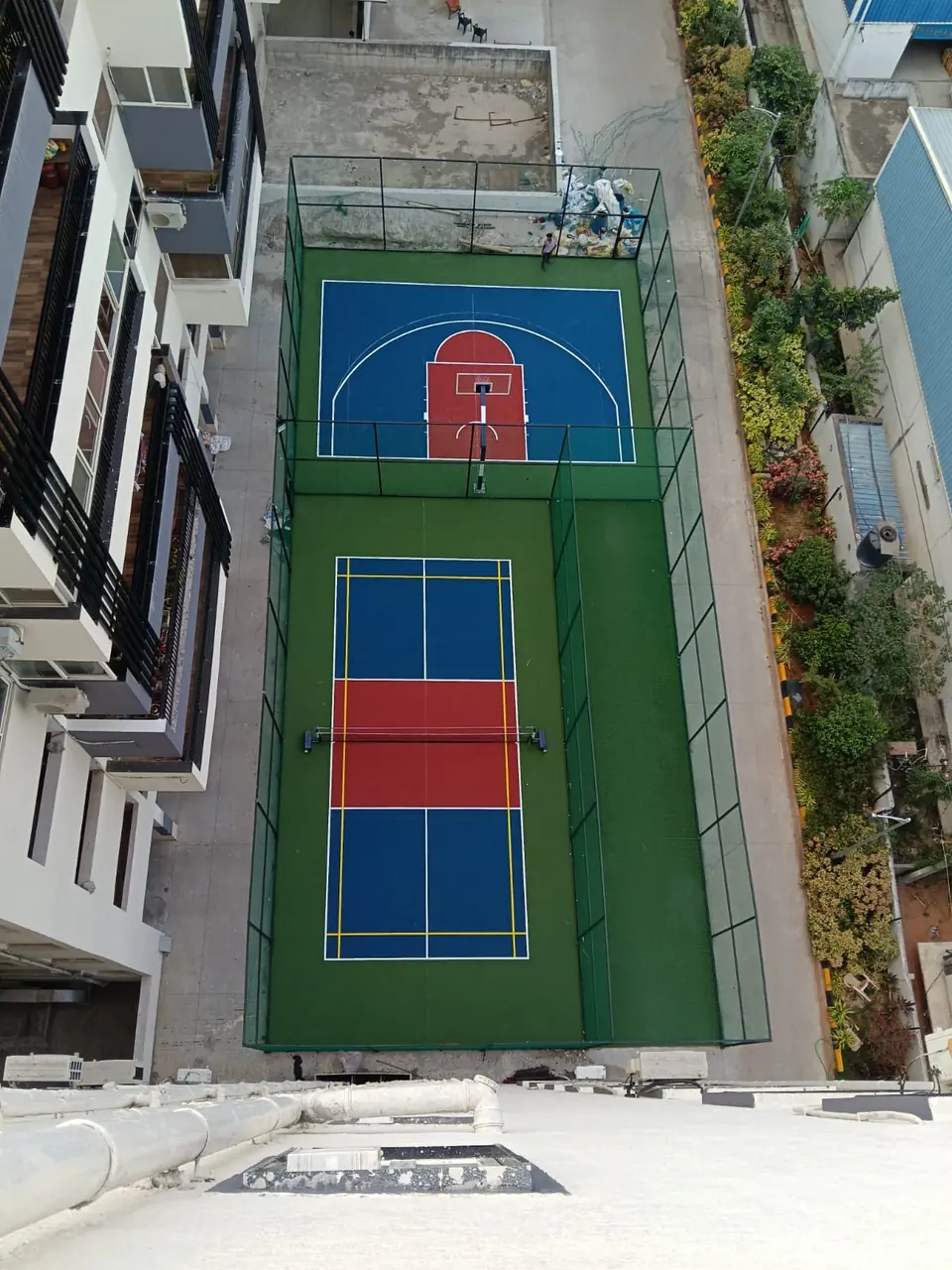Aerial view of a pickleball court and a half basketball court laid end to end between residential towers.