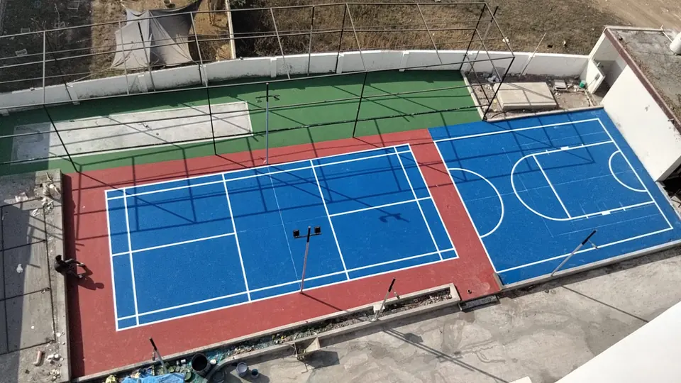 Rooftop sports area with an outdoor badminton court beside a half basketball court, in blue with a red surround.