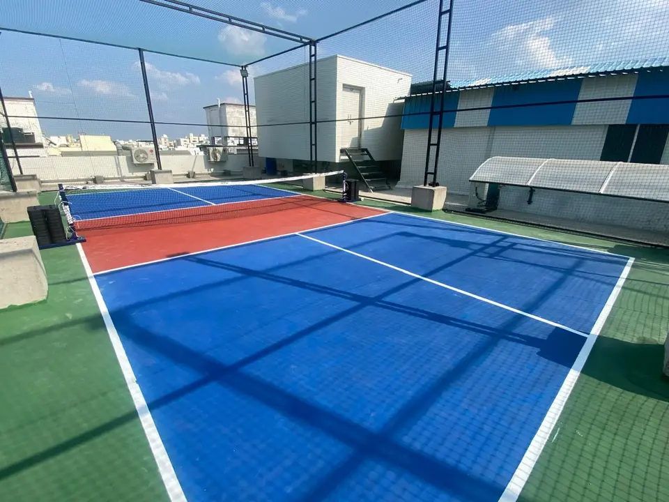 Rooftop pickleball court laid with blue, red and green interlocking sports tiles, enclosed by safety netting.