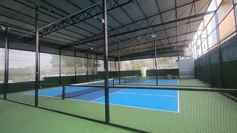 Two of the Rayadurgam indoor pickleball courts separated by tall netting on black steel posts, under the shed roof.