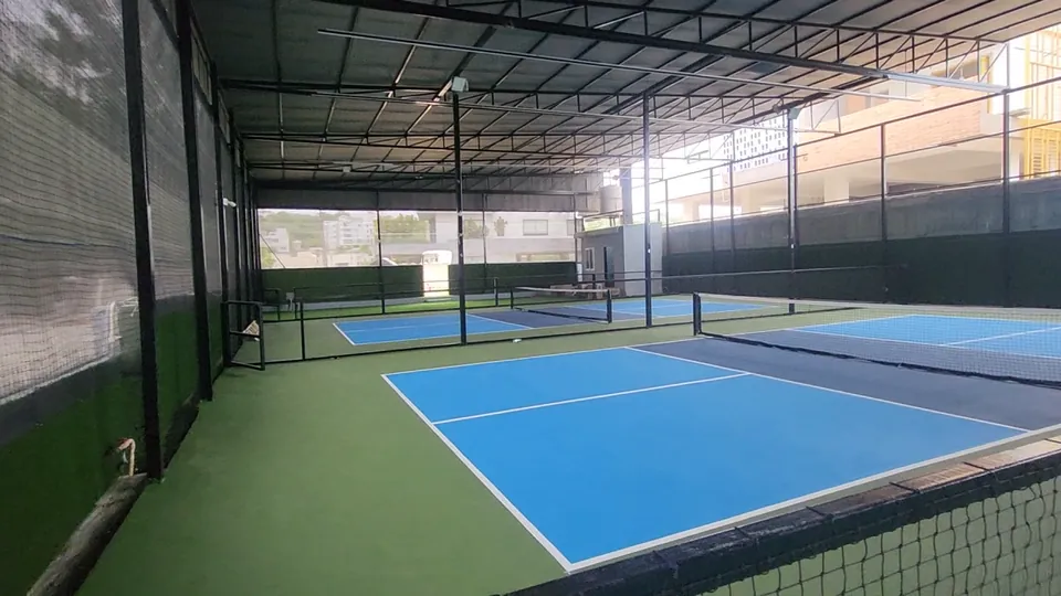 Pickleball courts at Rayadurgam seen along the length of the steel shed, with dividing nets, roof trusses and lighting above.