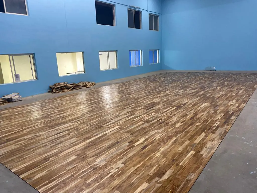Teak court floor in a blue indoor hall with a row of high windows, photographed after finishing.