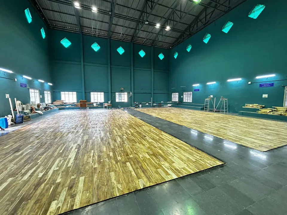Indoor wooden badminton courts in teak, laid by Kelysports on a stone floor in a teal hall with diamond-shaped windows.