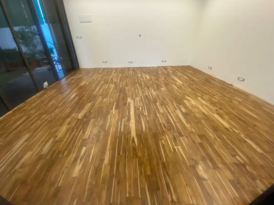 Polished teak wooden floor in a white room with full-height glass sliding doors.