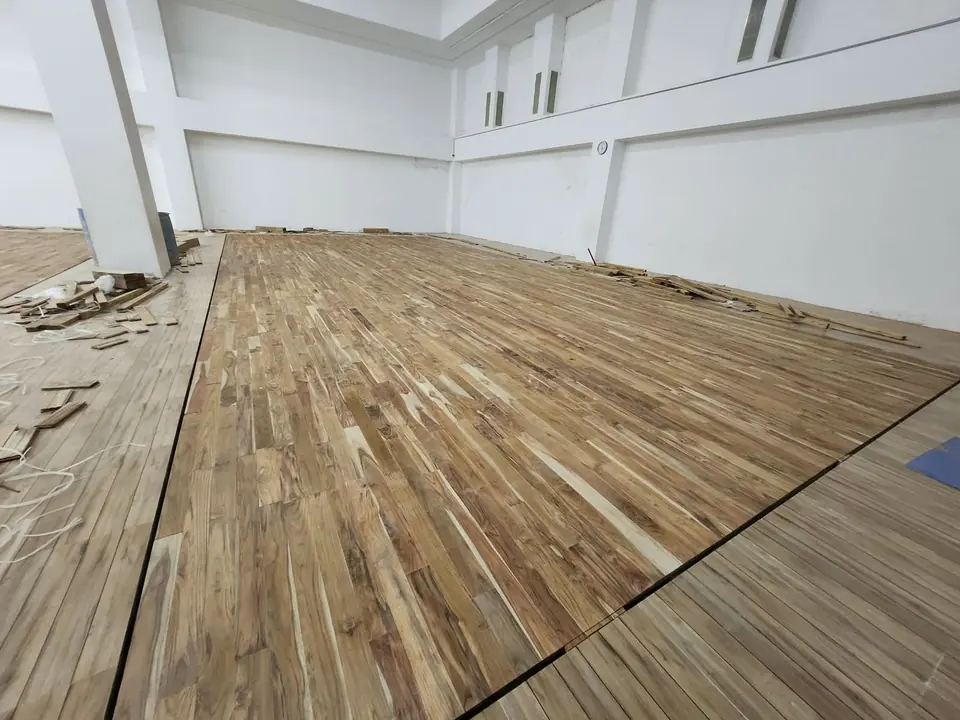 Teak wooden court flooring part-way through installation in a white hall, with timber offcuts along the edge.