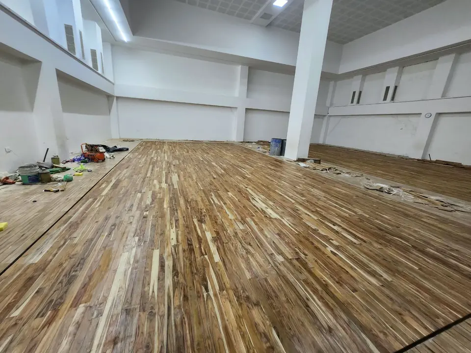 Newly laid teak floor boards in a white hall with a structural pillar, with tools and offcuts in the foreground.