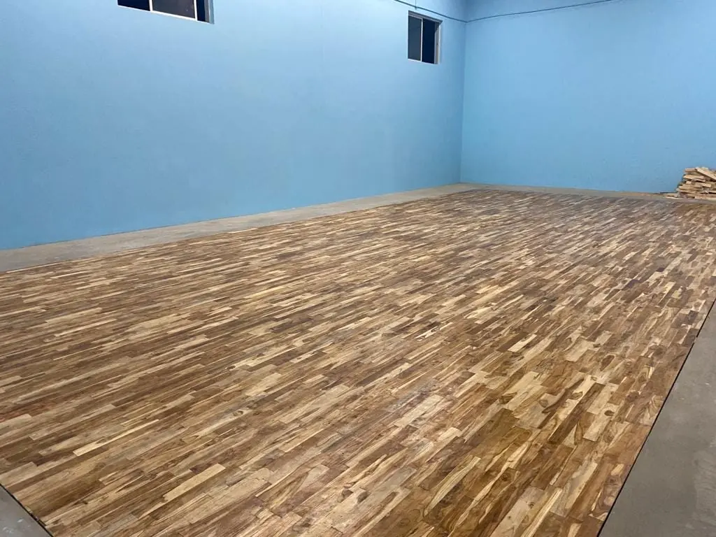 Glossy lacquered teak sports floor stretching across a blue-walled hall, seen from one corner.